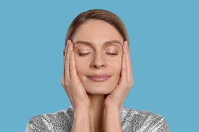 Photo of Woman massaging her face on turquoise background