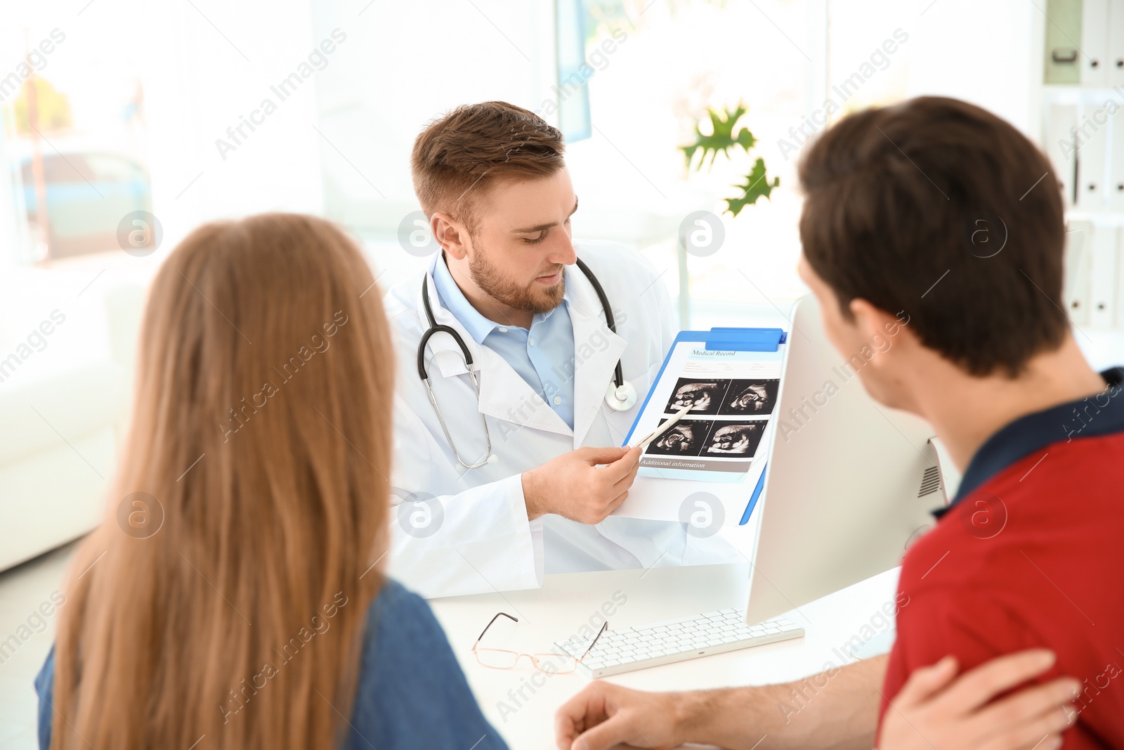 Photo of Gynecology consultation. Doctor showing ultrasound of baby to future parents in clinic