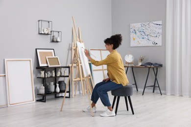 Photo of Young woman painting on easel with canvas in studio