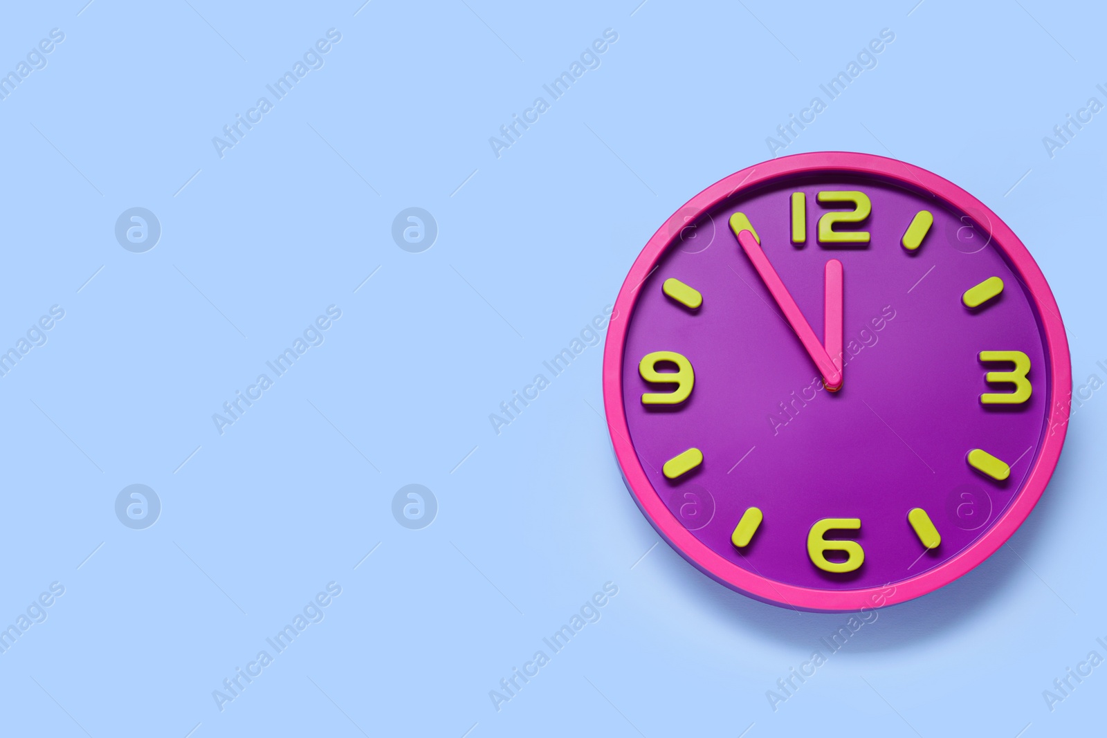 Photo of Clock showing five minutes until midnight on light blue background, top view with space for text. New Year countdown