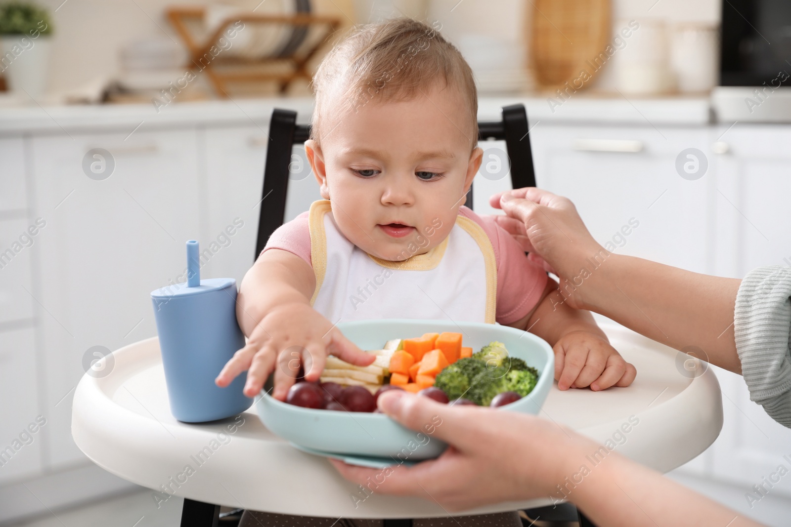 Photo of Mother feeding her cute little baby in kitchen