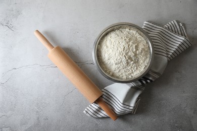 Photo of Flour in bowl, rolling pin and napkin on grey table, top view