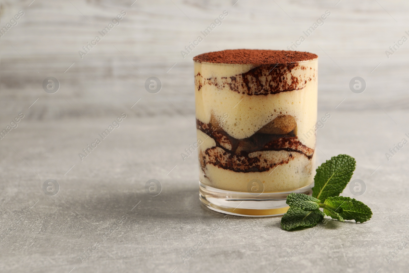 Photo of Delicious tiramisu in glass and mint on grey textured table, closeup. Space for text