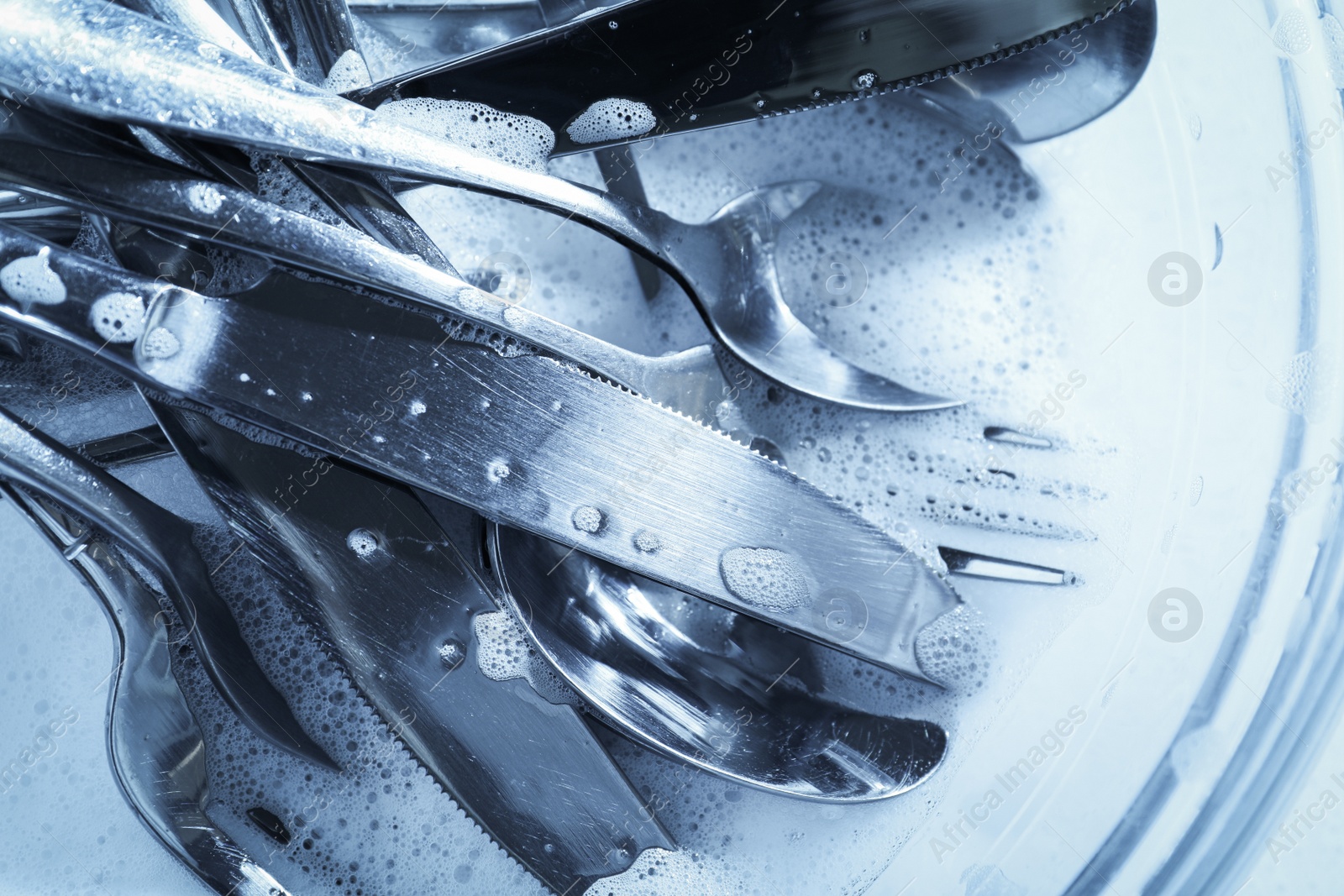 Photo of Glass bowl with silverware in foam, top view. Toned in blue