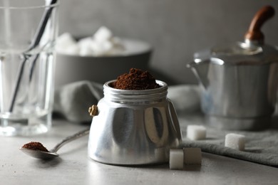 Ground coffee in moka pot and sugar cubes on light grey table, closeup