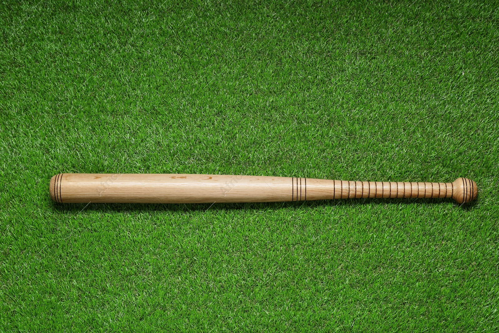 Photo of Wooden baseball bat on green grass, top view. Sports equipment