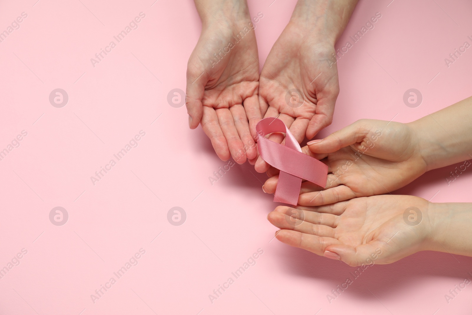 Photo of Breast cancer awareness. Women holding pink ribbon on color background, top view. Space for text