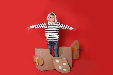 Photo of Little child playing with plane made of cardboard box on red background