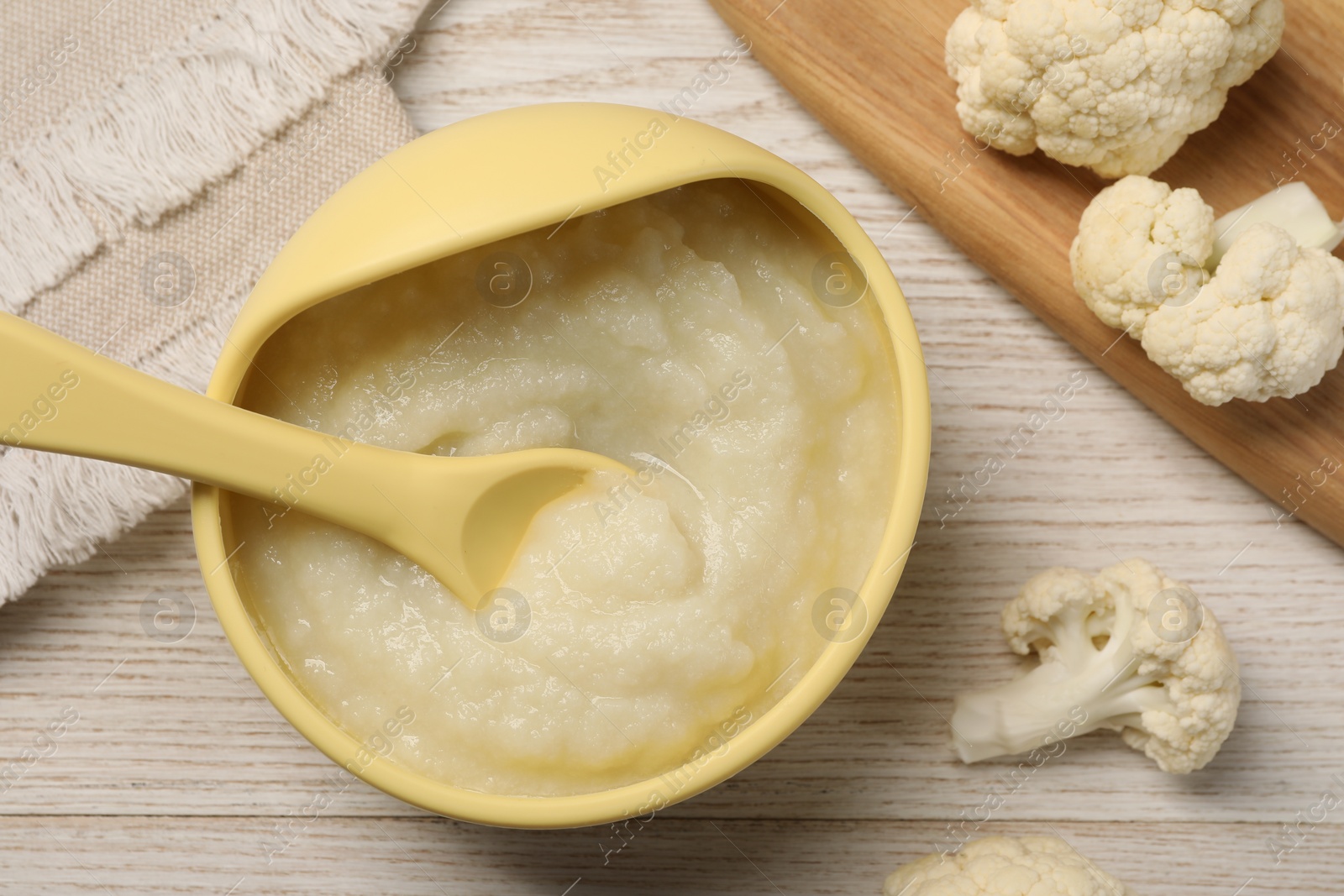 Photo of Baby food. Bowl with tasty cauliflower puree on light wooden table, flat lay