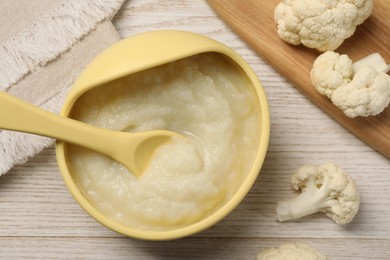 Photo of Baby food. Bowl with tasty cauliflower puree on light wooden table, flat lay