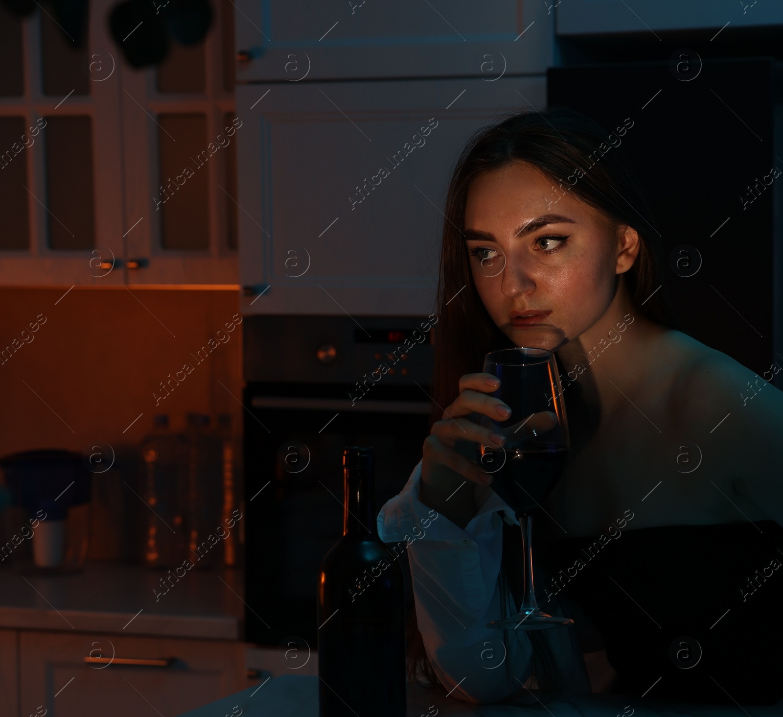 Photo of Beautiful woman chilling with glass of wine in kitchen at night