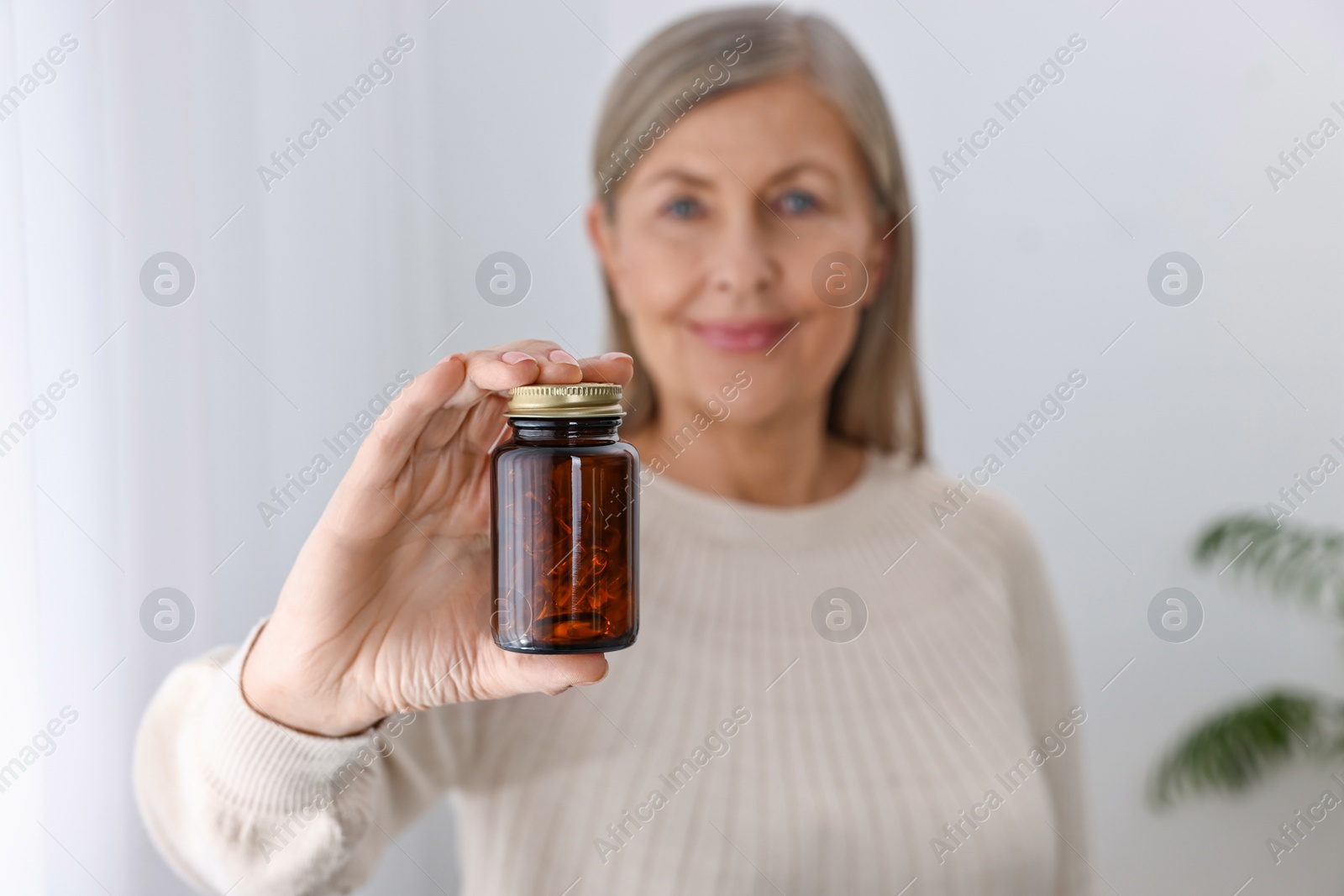 Photo of Beautiful woman holding jar of vitamin pills at home, selective focus