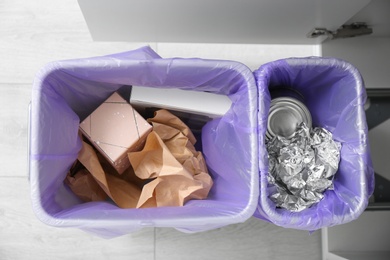 Open cabinet with full trash bins for separate waste collection in kitchen, top view