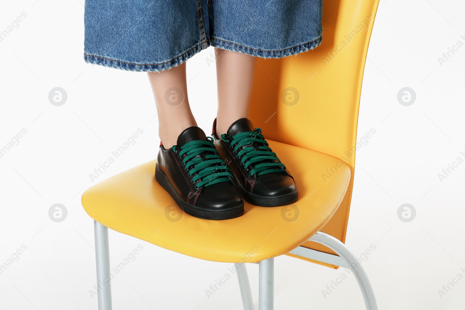 Photo of Woman in stylish shoes standing on chair against white background, closeup