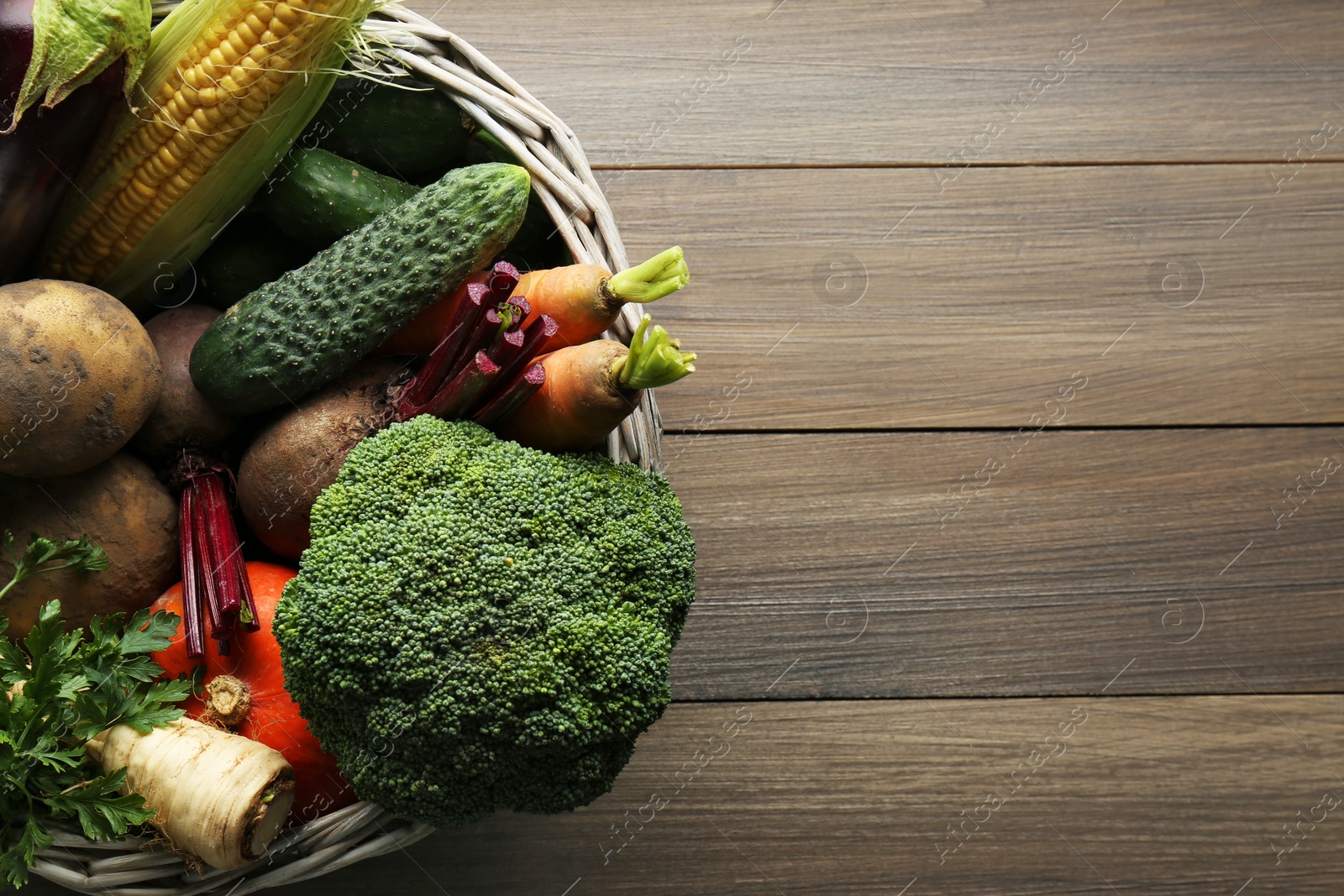 Photo of Basket with different fresh ripe vegetables on wooden table, top view. Space for text