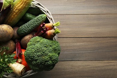 Basket with different fresh ripe vegetables on wooden table, top view. Space for text