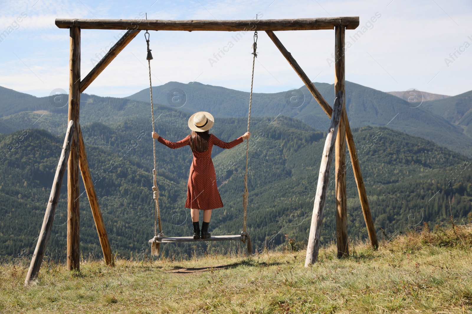 Photo of Young woman on outdoor swing in mountains, back view