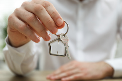 Real estate agent holding house key with trinket, closeup