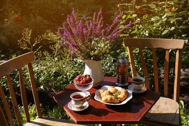 Photo of Beautiful bouquet of wildflowers, croissants and ripe strawberries on table served for tea drinking in garden