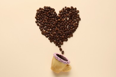 Photo of Coffee beans spilled from edible biscuit cup in shape of heart on beige background, top view