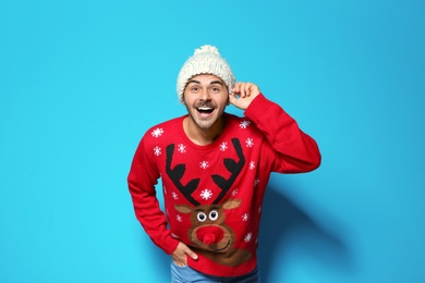 Young man in Christmas sweater and knitted hat on color background