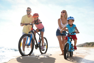 Happy parents teaching children to ride bicycles on sandy beach near sea