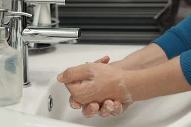 Photo of Man washing hands with soap over sink in bathroom, closeup