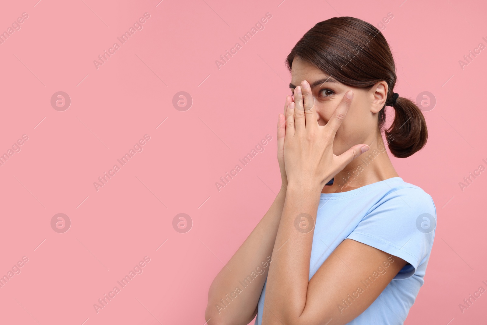 Photo of Embarrassed woman covering face with hands on pink background, space for text