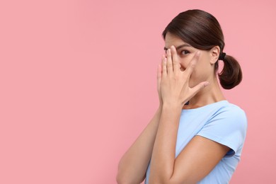 Photo of Embarrassed woman covering face with hands on pink background, space for text
