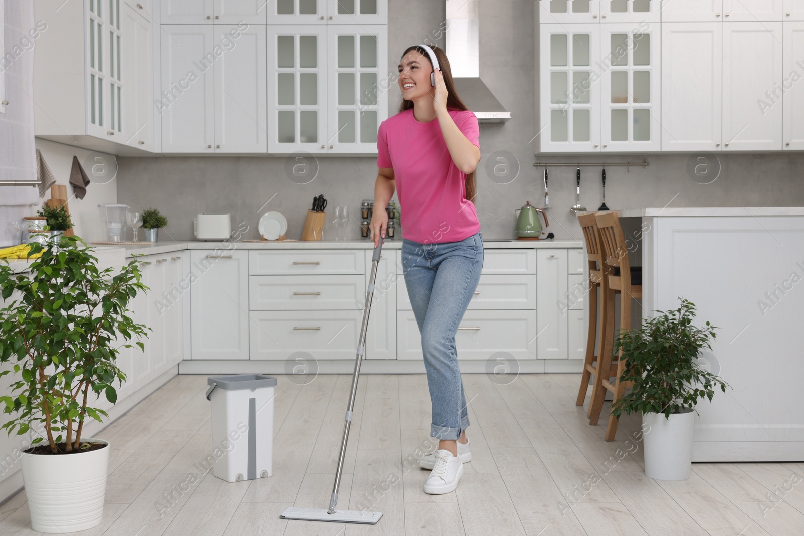 Photo of Enjoying cleaning. Happy woman in headphones listening music and mopping floor in kitchen