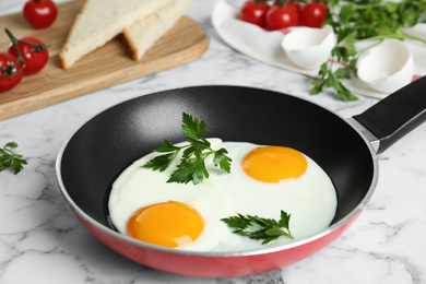 Photo of Tasty cooked chicken eggs with parsley in frying pan on white marble table, closeup