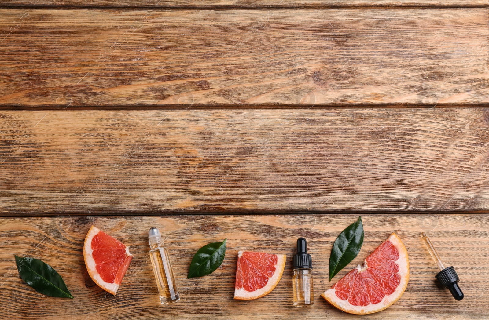 Photo of Flat lay composition with grapefruit slices and bottles of essential oil on wooden background, space for text