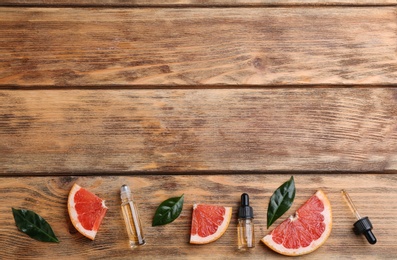 Flat lay composition with grapefruit slices and bottles of essential oil on wooden background, space for text