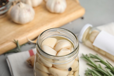 Photo of Jar of pickled garlic on grey table, closeup