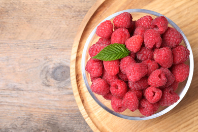 Photo of Delicious fresh ripe raspberries in bowl on wooden table, top view. Space for text