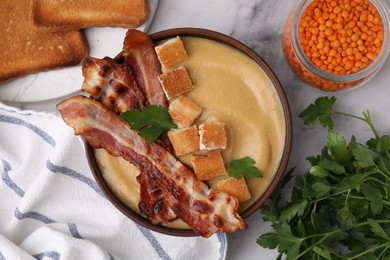 Photo of Delicious lentil soup with bacon and parsley in bowl on light marble table, flat lay