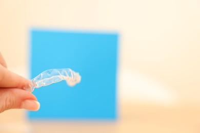 Photo of Woman with transparent dental aligner on blurred background, closeup. Space for text