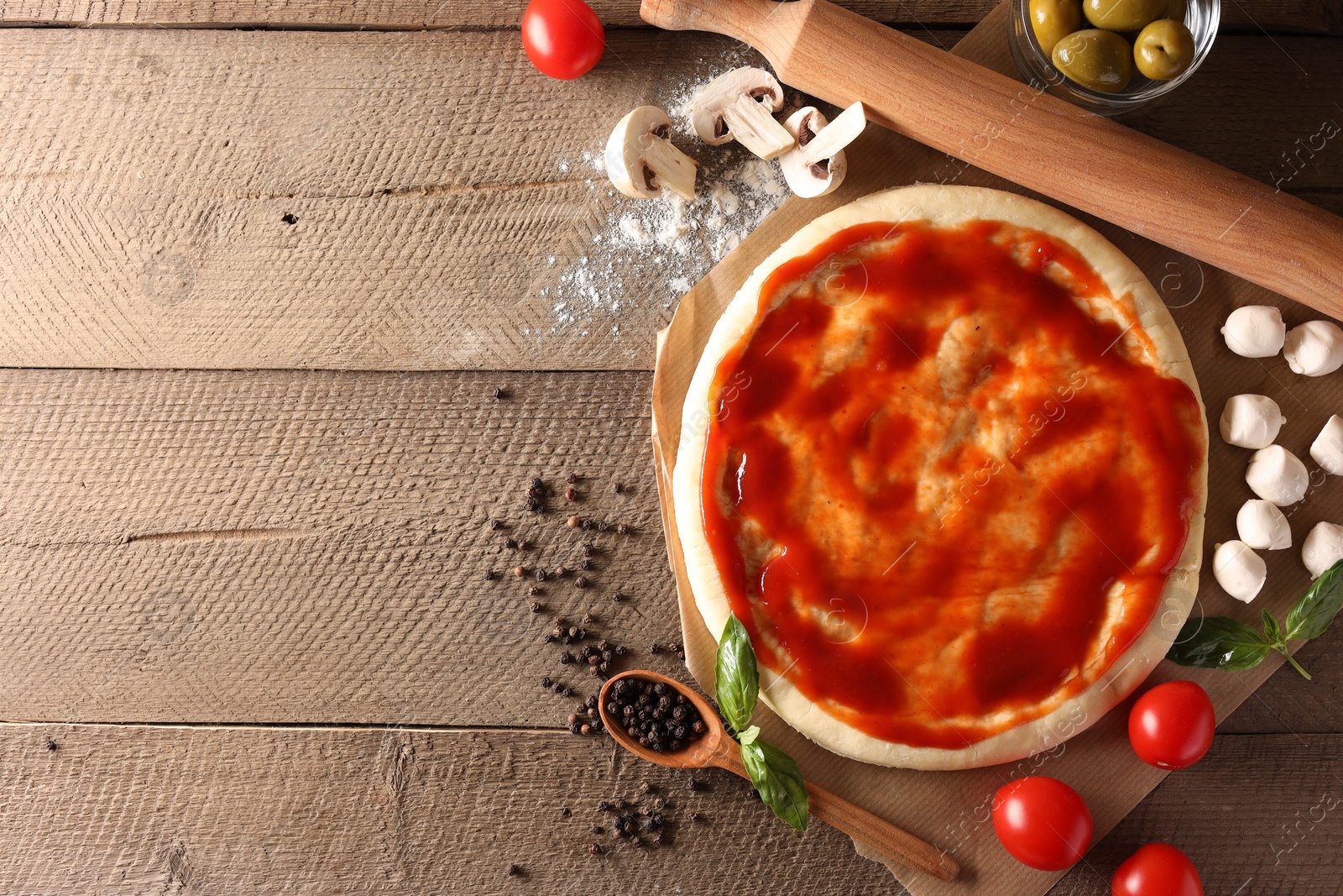 Photo of Pizza dough smeared with tomato sauce, products and rolling pin on wooden table, flat lay. Space for text