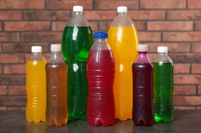 Photo of Bottles of soft drinks with water drops on table near brick wall