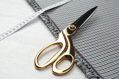 Photo of Scissors, fabric and measuring tape on white wooden table, closeup