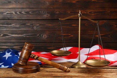 Photo of Scales of justice and gavel on wooden table against American flag