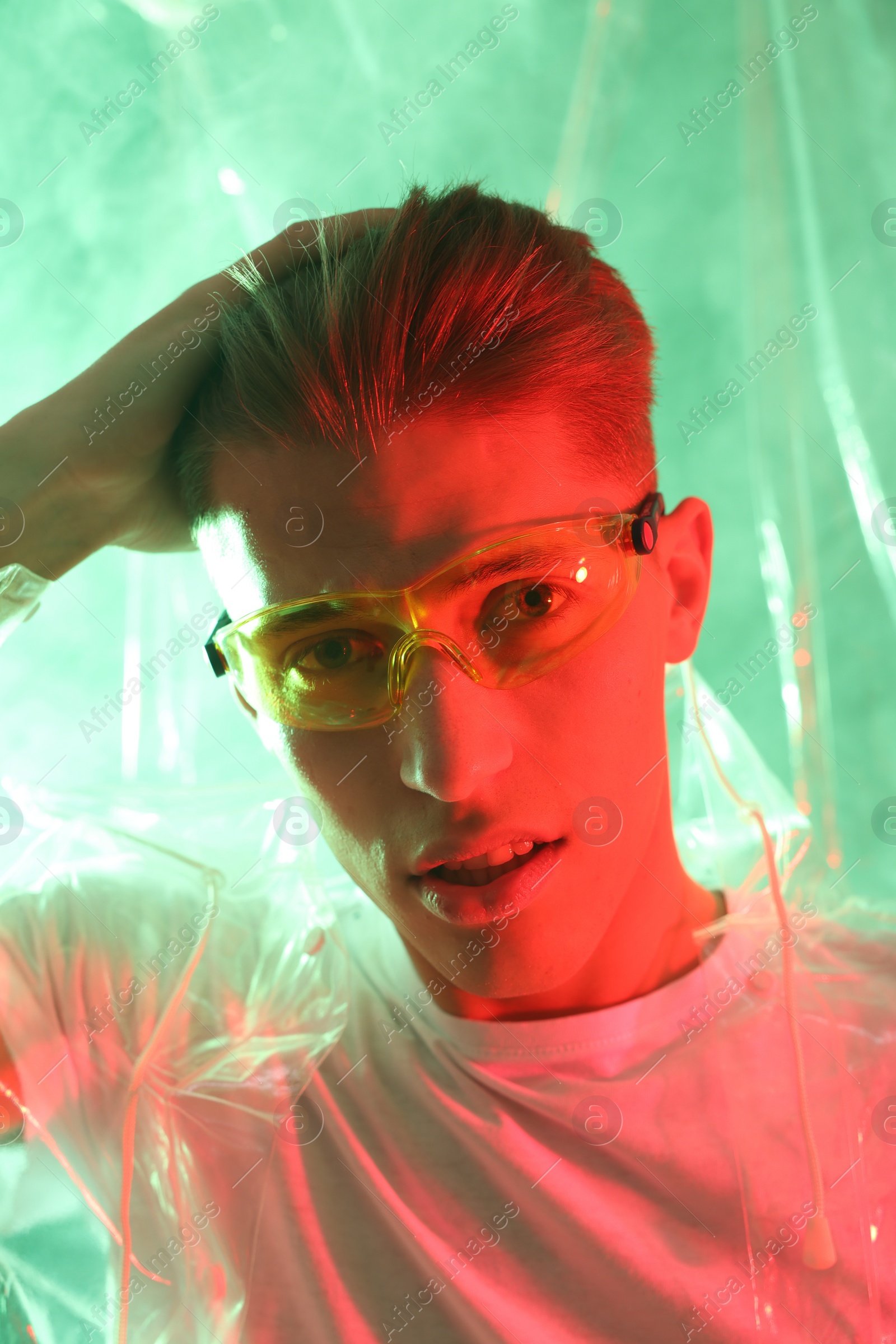 Photo of Stylish young man wearing clear coat and glasses in neon lights