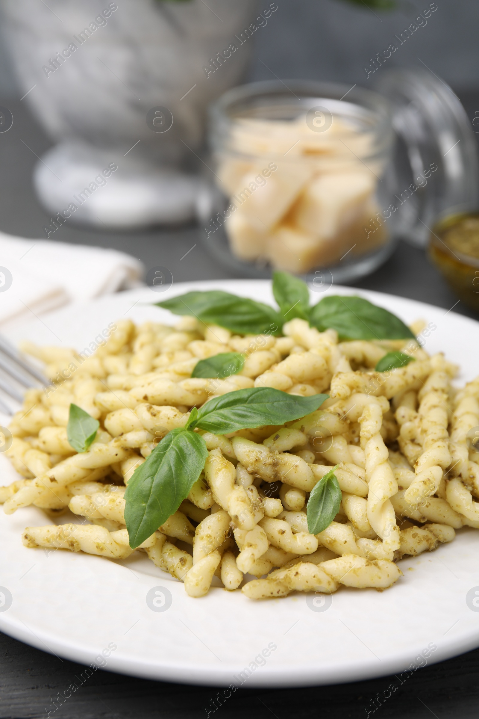 Photo of Plate of delicious trofie pasta with pesto sauce and basil leaves on grey wooden table, closeup