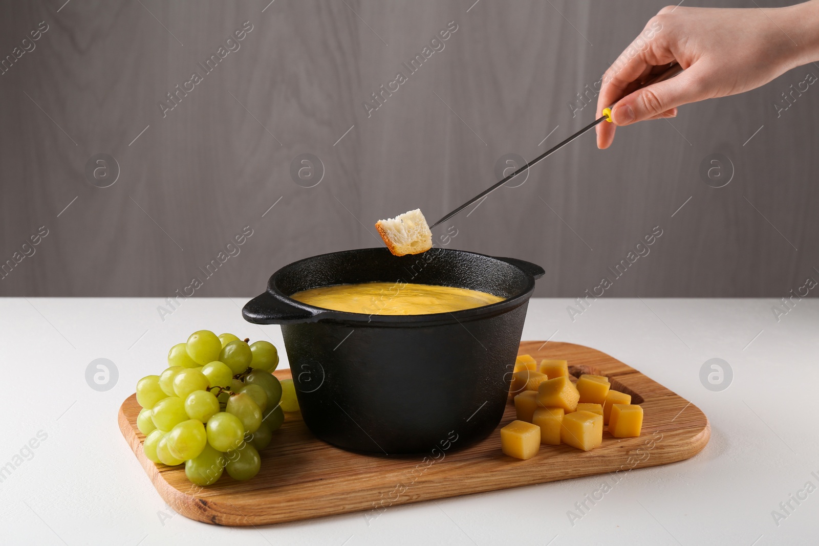 Photo of Woman dipping piece of bread into fondue pot with tasty melted cheese at white table, closeup