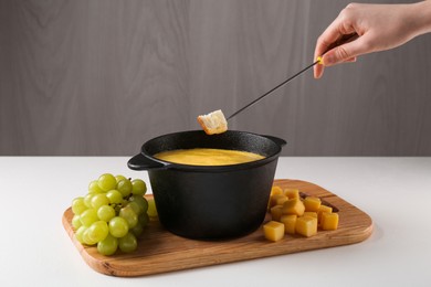 Woman dipping piece of bread into fondue pot with tasty melted cheese at white table, closeup