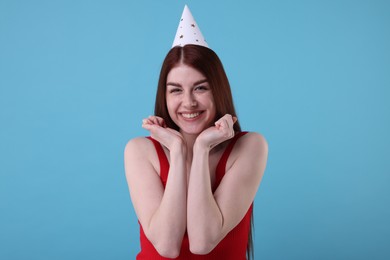 Happy woman in party hat on light blue background