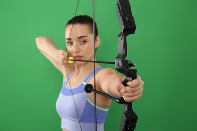Photo of Young woman practicing archery against green background, focus on bow