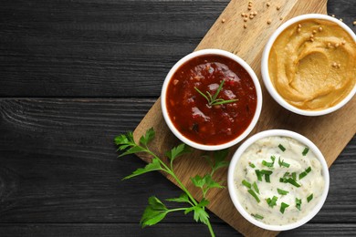 Different tasty sauces in bowls and parsley on black wooden table, top view. Space for text