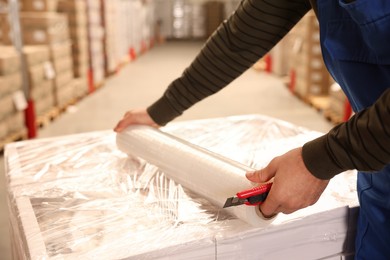 Worker wrapping boxes in stretch film at warehouse, closeup