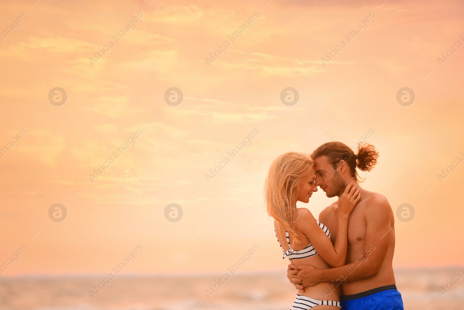 Photo of Young woman in bikini kissing her boyfriend on beach at sunset. Lovely couple